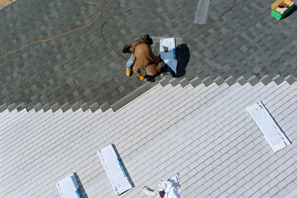 Aerial view of worker nailing new roof shingles with bitumen using an air hammer
