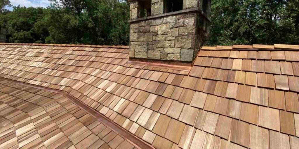 Newly installed cedar wood shake roof with stone chimney on a residential home surrounded by trees