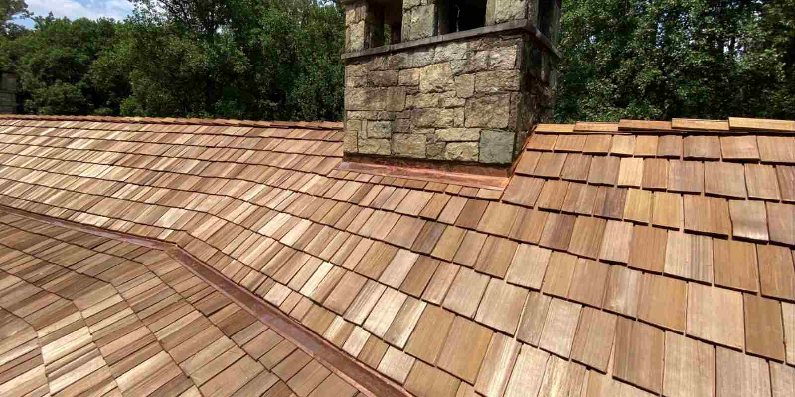 Newly installed cedar wood shake roof with stone chimney on a residential home surrounded by trees