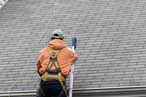 house during day with gray color single family home and man walking on roof shingles and ladder during repair