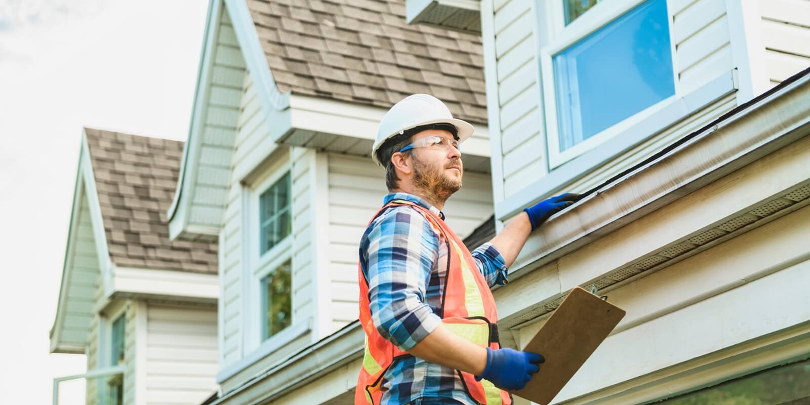 man with hard hat standing on steps inspecting house roof