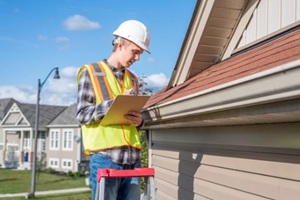 home inspector standing on a ladder and providing an inspection to the roof of a house